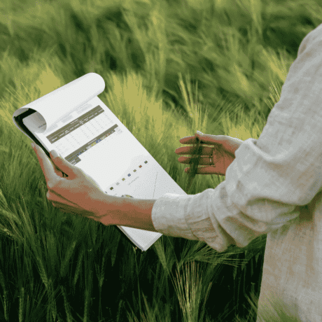 Image of a woman inspecting a green crop and holding a clip board